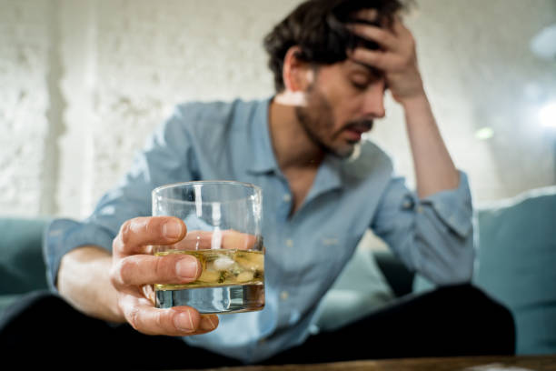 drunk alcoholic lain business man drinking whiskey from the bottle and glass depressed wasted and sad at home couch in alcohol abuse and alcoholism concept stock photo