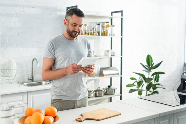 istock adult smiling man with digital tablet looking for recipe near table on kitchen 1001401332