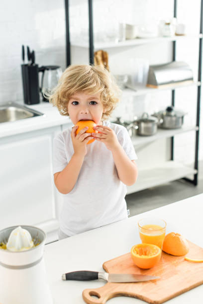 istock little boy eating orange near table with cutting board and knife on kitchen 1001401484