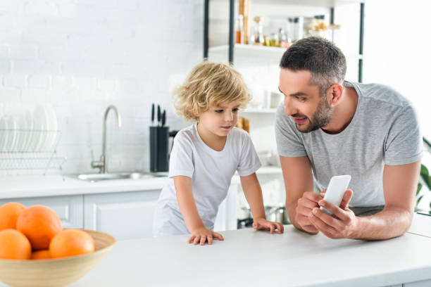 istock smiling father showing smartphone to little son at kitchen 1001401504