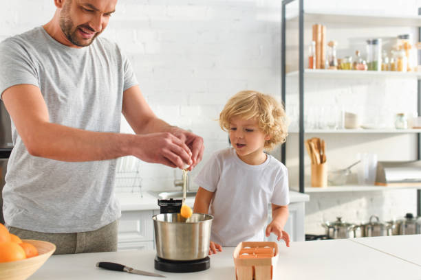 istock adorable boy looking how his father breaking egg into bowl at kitchen 1001401606
