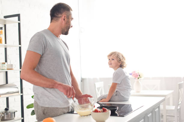 istock father whisking dough in bowl and talking to son while he sitting on tabletop at kitchen 1001401956