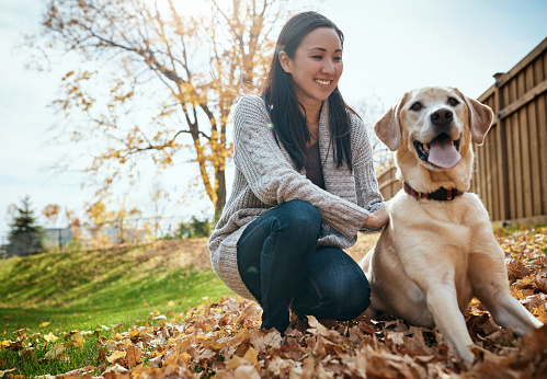 Shot of an attractive young woman having fun with her dog on an autumn day in a garden