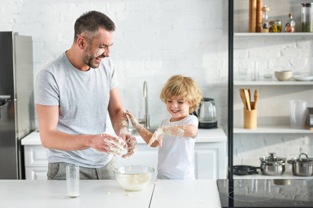 istock laughing father and son having fun while making dough in bowl at kitchen 1001405380