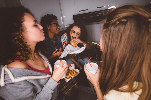 Happy multi-ethnic friends and roommates having fun at college dorm party eating fast food