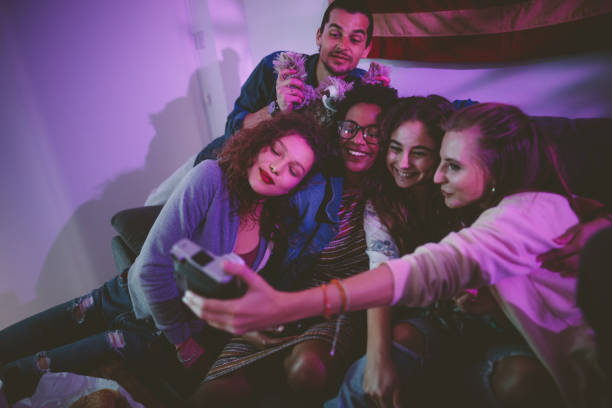 Smiling multi-ethnic friends taking selfie at home with vintage camera Happy multi-ethnic teenage friends taking polaroid selfies on instant photo camera at house party college dorm party stock pictures, royalty-free photos & images
