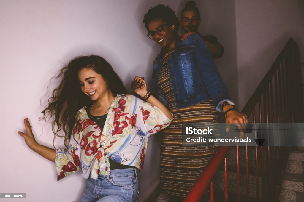 Happy multi-ethnic mischievous teenagers running down staircase Multi-ethnic teenage friends sneaking out house and running down staircase after mischief Party - Social Event Stock Photo