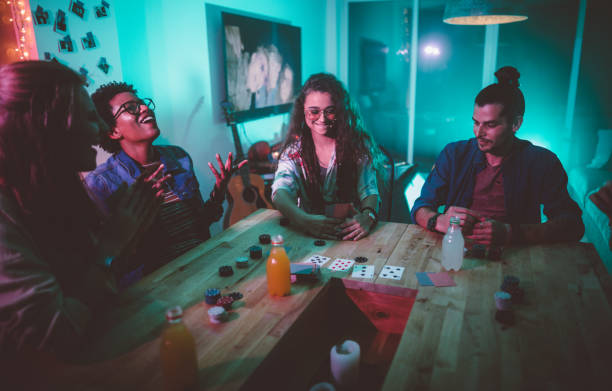 Multi-ethnic hipster friends playing cards game at college dorm party Multi-ethnic hipster teenage friends having fun gambling and playing poker game while hanging out together college dorm party stock pictures, royalty-free photos & images