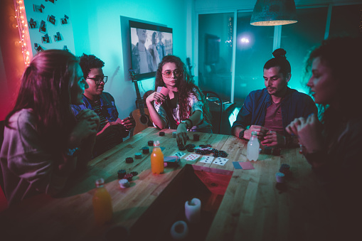Multi-ethnic hipster friends hanging out and playing cards game with chips at college dorm