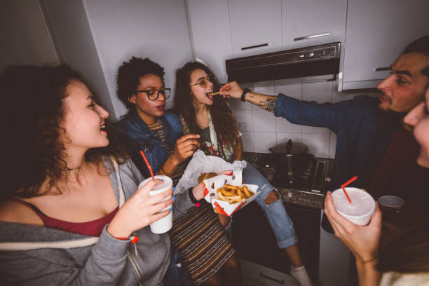 Happy multi-ethnic teenage friends partying and eating fast food Young multi-ethnic hipster friends having fun at college dorm party and eating fast food college dorm party stock pictures, royalty-free photos & images