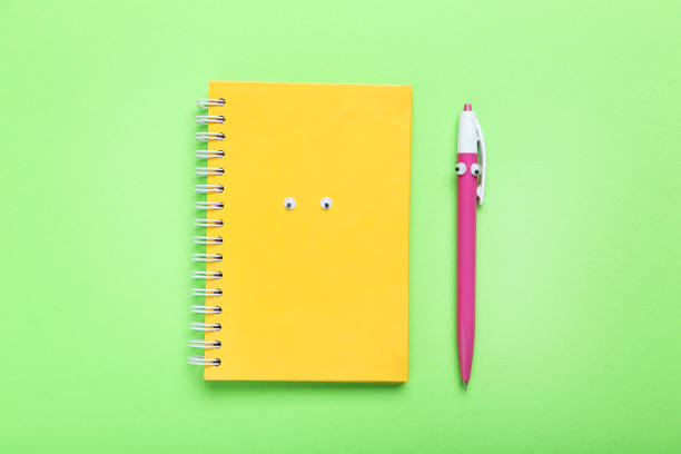 Notebook and pen with googly eyes on a green background