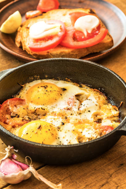 istock Fried eggs with tomatoes in a cast-iron frying pan on an old wooden table 1001427432