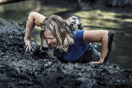 Individual beautiful blonde woman having sporty fun at a public mud run obstacle course