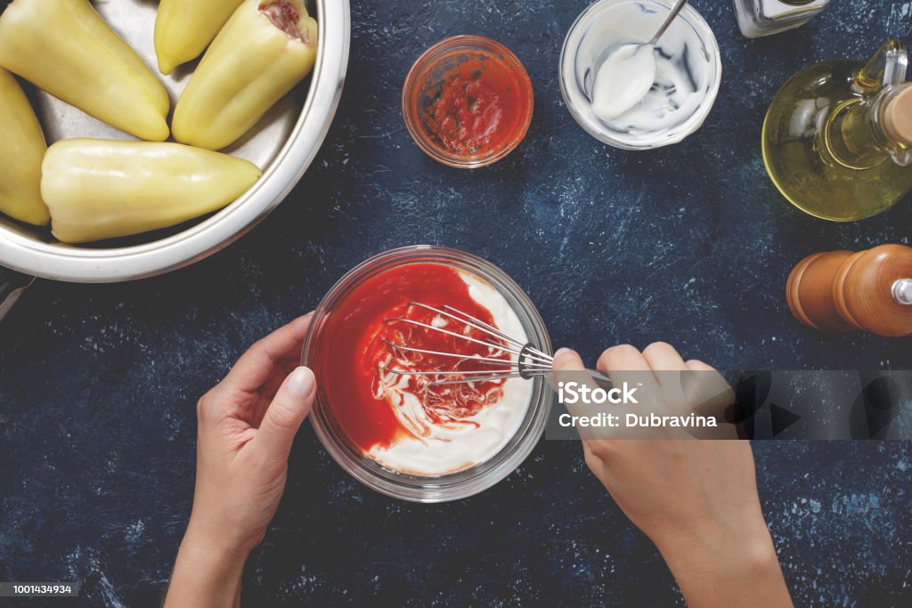 Hands mixing tomato sauce and sour cream in glass bowl for making filled paprika. Hands mixing tomato sauce and sour cream in glass bowl for making filled paprika. Step by step recipe of homemade stewed stuffed sweet pepper top view. Mixing Stock Photo