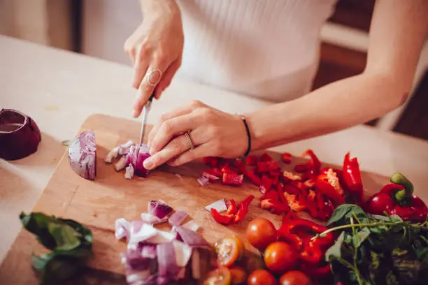 Close-up of woman cutting fresh vegetables while cooking healthy Mediterranean lunch in house kitchen