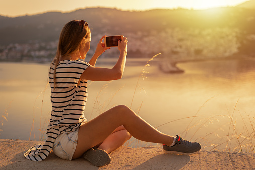 Woman taking a sunset photo of the island with her smart phone