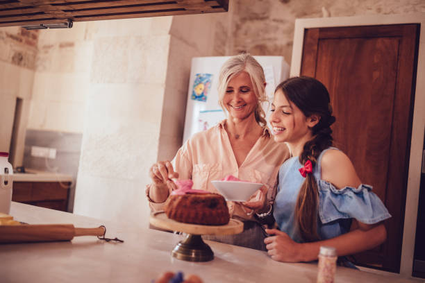 istock Granddaughter helping grandmother with baking and icing cake in kitchen 1001451216
