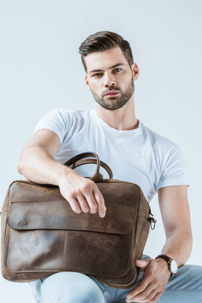 istock Stylish young man sitting and holding briefcase isolated on white background 1001473416