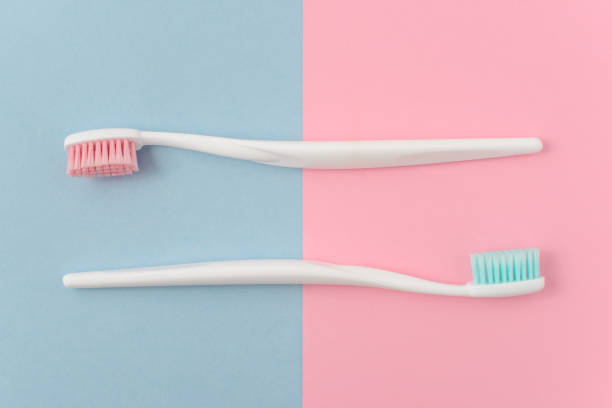 primo piano di due spazzolini bianchi di plastica con setola rosa e blu su sfondo rosa e blu. spazio di copia gratuito. - toothbrush pink turquoise blue foto e immagini stock