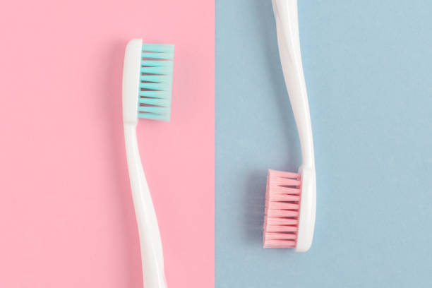 zbliżenie dwóch plastikowych białych szczoteczek do zębów z różowym i niebieskim włosiem na różowym i niebieskim tle. wolne miejsce na kopiowanie. - toothbrush pink turquoise blue zdjęcia i obrazy z banku zdjęć