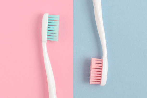 perto de duas escovas de dente brancas plásticas com cerdas rosa e azul sobre fundo azul e rosa. espaço de cópia gratuita. - toothbrush pink turquoise blue - fotografias e filmes do acervo