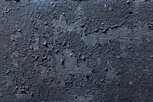 Texture of black coloured metal background with a peeling cracked layers of paint.