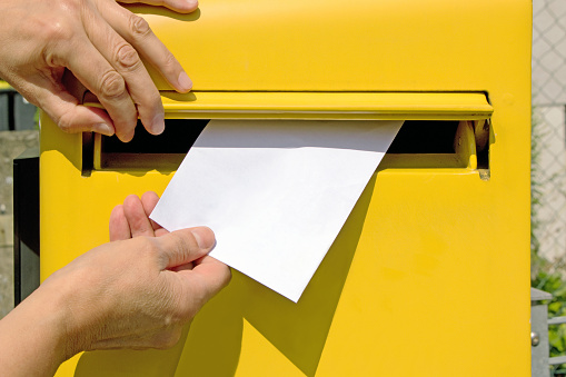 hands dropping blank envelope into a post box