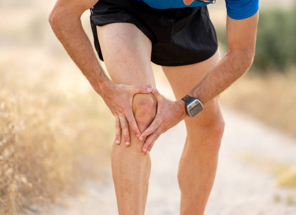 young sport man with strong athletic legs holding knee with his hands in pain after suffering muscle injury during a running workout training in asphalt road in muscular or ligament injury concept. hombre de deporte joven con fuertes piernas atléticas sosteniendo la rodilla con sus manos en el dolor después de sufrir lesión muscular durante un entrenamiento de entrenamiento corriente en carretera asfaltada en muscular o concepto de lesiones de lig
