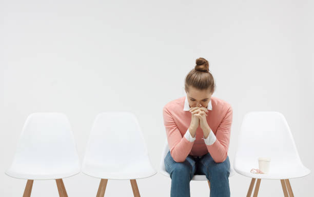 istock Young woman sitting in the line or queue, looking stressed, putting hands together as if she is praying with closed eyes to overcome depression 1001503126