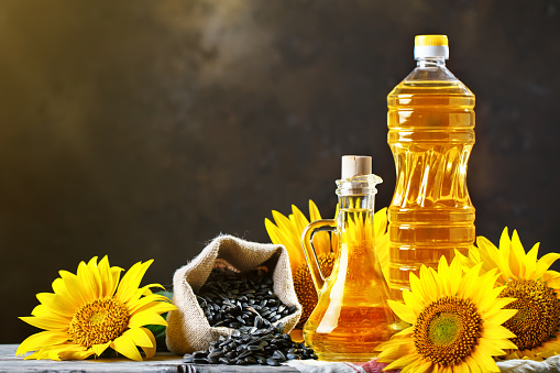 Closeup photo of sunflowers and sunflower oil with seeds on on a wooden table. Bio and organic concept of the product. Selective focus. Background with copy space.