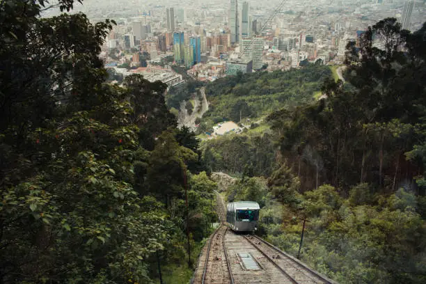 A funicular arrives at the teleferico system of monserrate in Bogota, which was opened in 1955, many buildings and trees can be seen behind, this dramatic shot shows the relationship between the mountain  and the city.