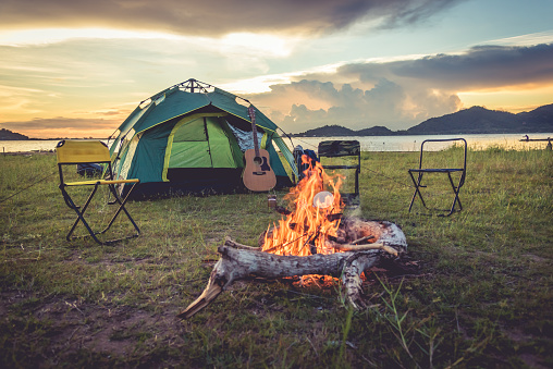 Camping tent with bonfire in the green field meadow, Lake and mountain background. Picnic and travel concept. Nature theme.