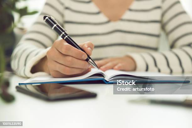 Young Business Woman Sitting At Table And Writing In Notebook On Table Is Smartphone And Tablet Freelancer Working Writing Down New Ideas Stock Photo - Download Image Now