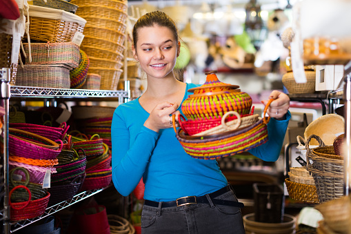 girl customer choosing multicolor wicker basket in decor items store
