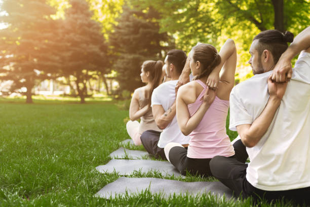 gruppe von menschen praktizieren yoga im park - yoga exercising outdoors group of people stock-fotos und bilder