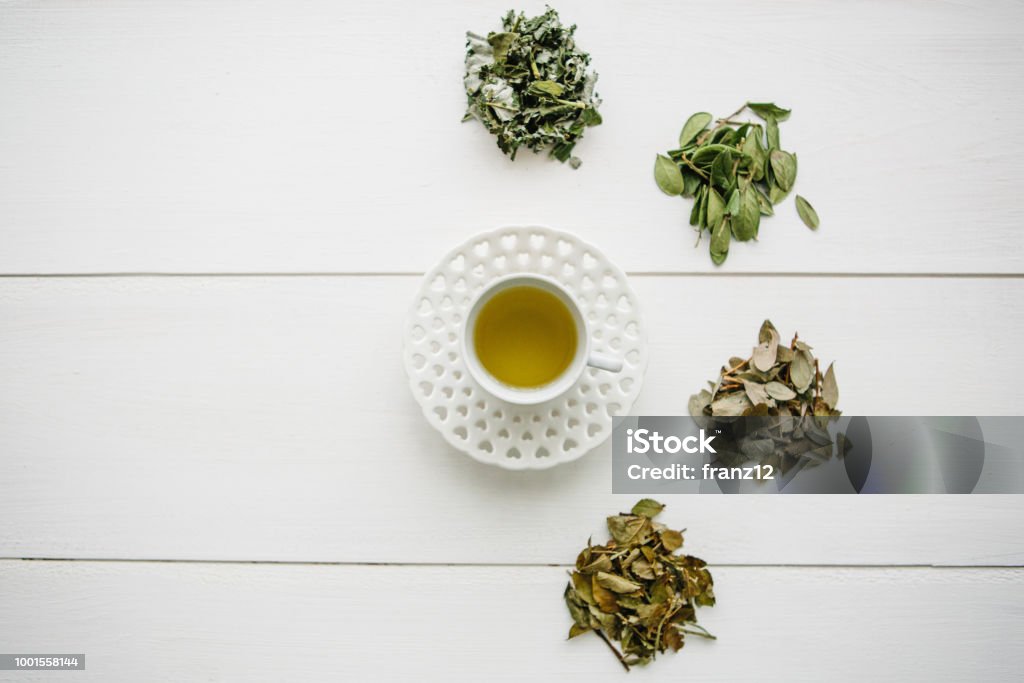 Fresh fragrant and healthy herbal tea in a glass or mug on a white wooden surface. Next to it lie various dried herbs for making tea. Healthy product Fresh fragrant and healthy herbal tea in a glass or mug on a white wooden surface. Next to it lie various dried herbs for making tea. Healthy product. Above Stock Photo