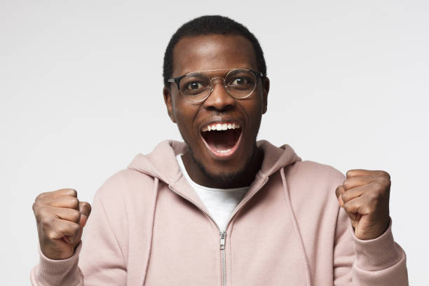 istock Young black male shouting while his team win, raised both fist in victory gesture, isolated on gray background 1001563444