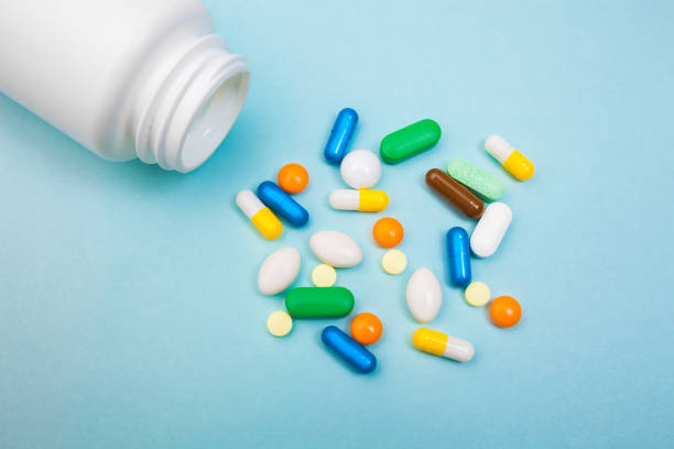 istock Multi-colored tablets and capsules, white bottle for tablets, pharmaceutical medicine pills on blue background, an analgesic against diseases 1001571202