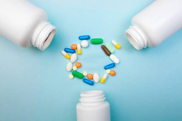 istock Multi-colored tablets and capsules, white bottle for tablets, pharmaceutical medicine pills on blue background, an analgesic against diseases 1001571254