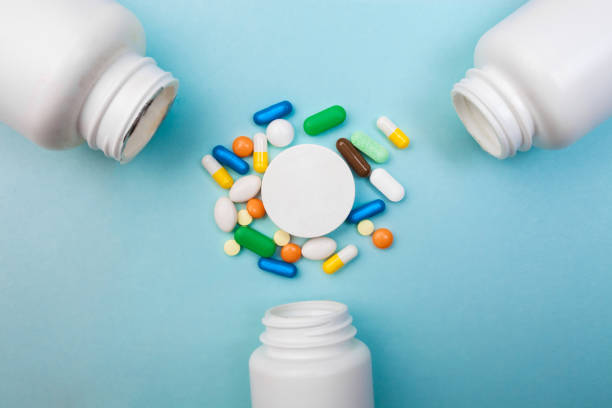 istock Multi-colored tablets and capsules, white bottle for tablets, pharmaceutical medicine pills on blue background, an analgesic against diseases 1001571268