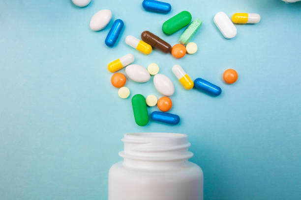 istock Multi-colored tablets and capsules, white bottle for tablets, pharmaceutical medicine pills on blue background, an analgesic against diseases 1001571272