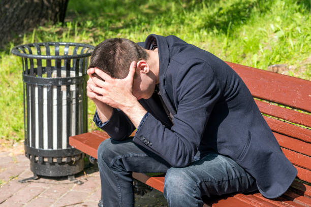 istock young man sitting on bench in park, covering his face with his hands 1001576332