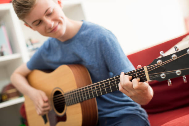 adolescent assis sur le canapé à la maison playing guitar - guitar child music learning photos et images de collection