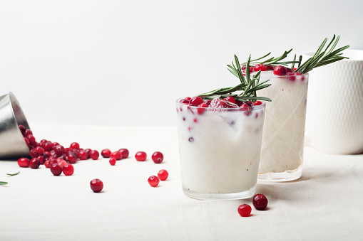 Refreshing drink for summer: two glasses of cold refreshing sangria with fruits arranged all around the glasses shot on white table. Fruits included in the composition are grape, orange, lime and berries. The sangria glasses are garnished with mint leaves. Two red and white drinking straws complete the composition. The composition is at the right of an horizontal frame leaving useful copy space for text and/or logo at the left. Predominant colors are red and white. High resolution 42Mp studio digital capture taken with Sony A7rII and Sony FE 90mm f2.8 macro G OSS lens