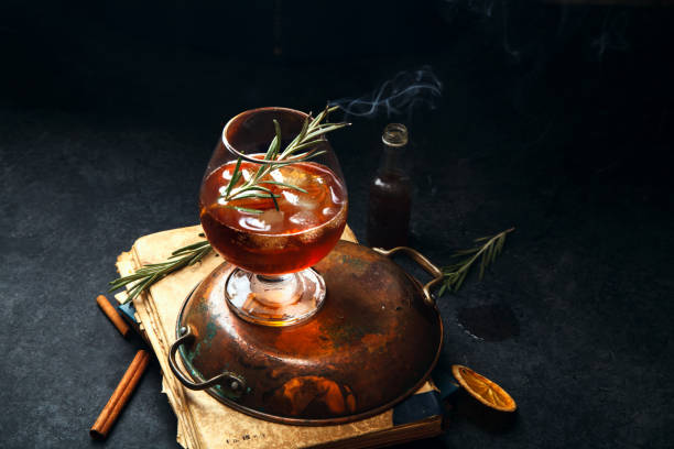 istock Whiskey cocktail with ice and burnt rosemary. Dark background, vintage papers, dramatic ligting. Horizontal composition with copy space. 1001584792
