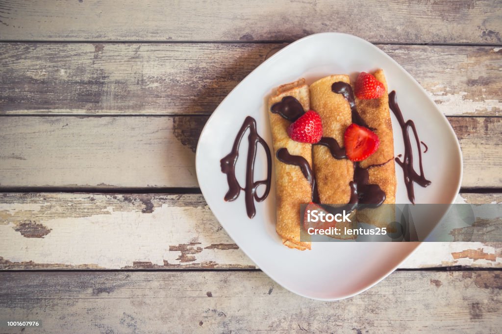 Crepes with fresh strawberries and chocolate syrop Crepes with fresh strawberries and chocolate syrop on aged wooden background. Top view. Backgrounds Stock Photo