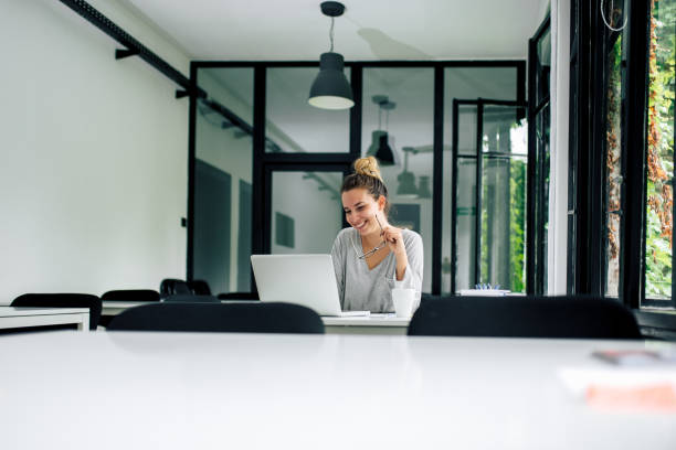 istock Smiling girl looking at laptop screen and holding eyeglasses at modern study room. Copy space. 1001611352