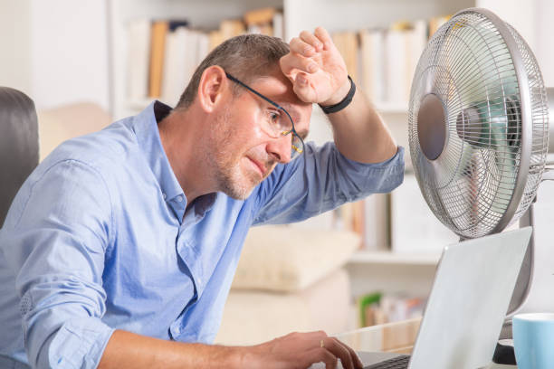 Man suffers from heat in the office or at home Man suffers from heat while working in the office and tries to cool off by the fan heat stress stock pictures, royalty-free photos & images