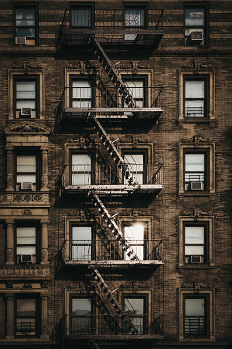 Facade of a typical New York block of flats with fire escape at the front, sun reflects in the windows.