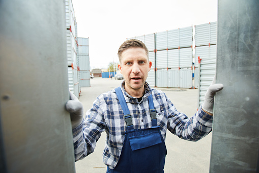 Shocked emotional handsome worker in overall opening metal container and discovering burglary at cargo storage area